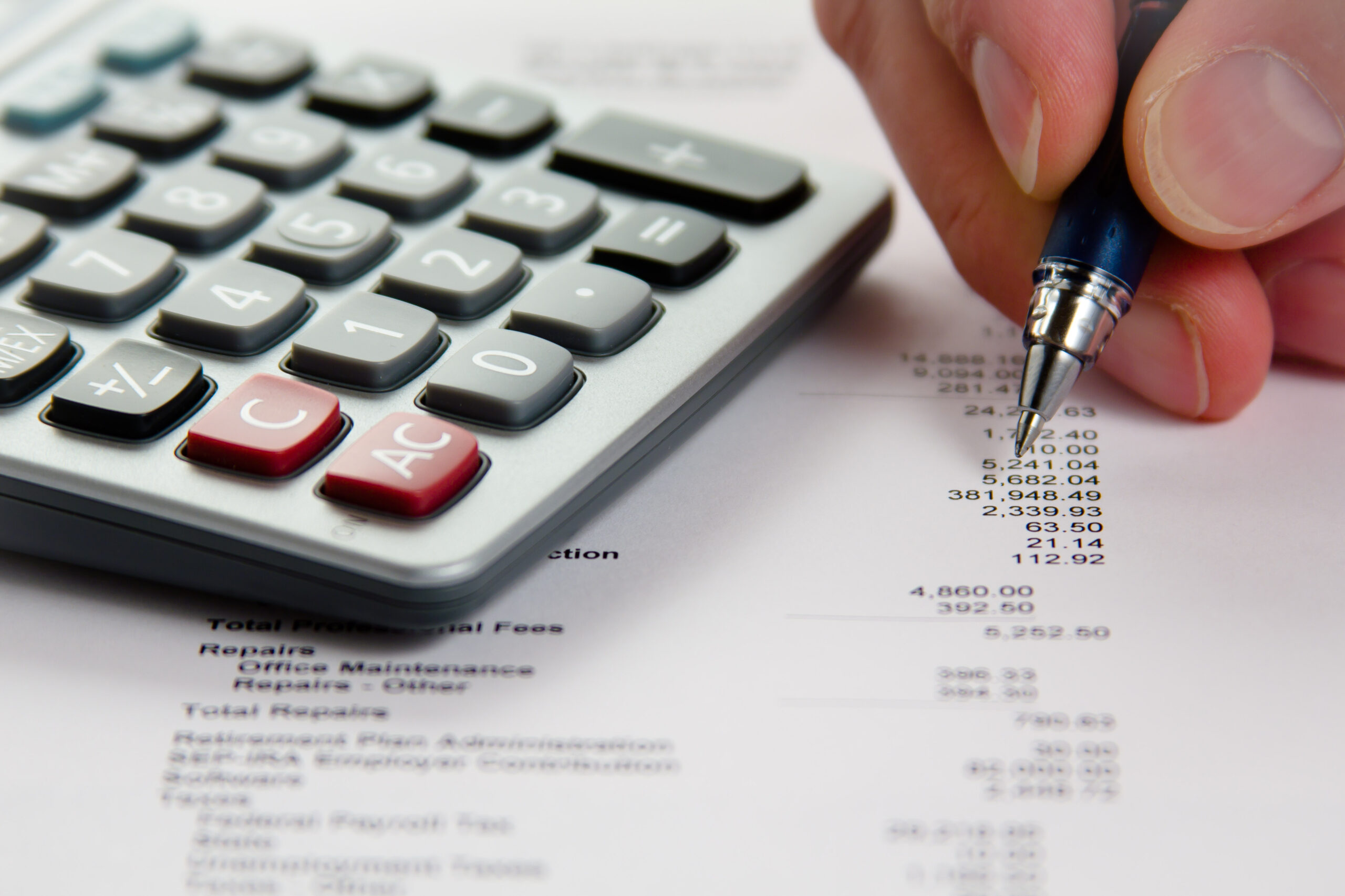 Close-up of a hand holding a pen beside a calculator and a printed financial statement.